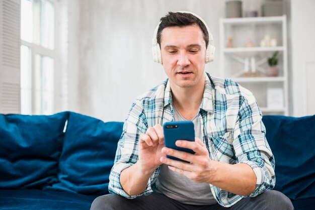 Man listening music in headphones and using smartphone on sofa