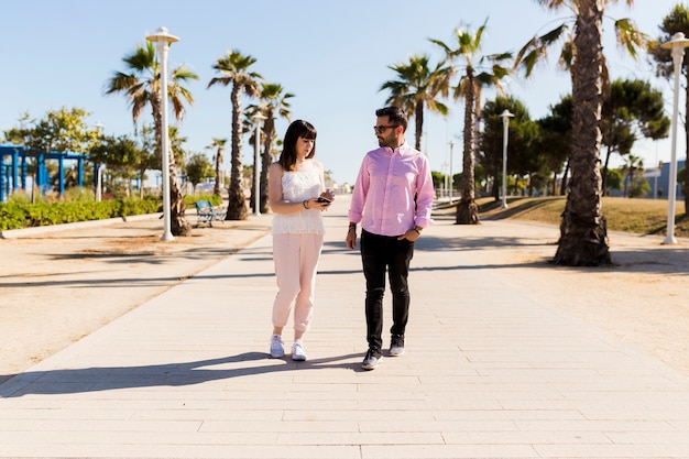 Man looking at beautiful young woman showing mobile phone on street