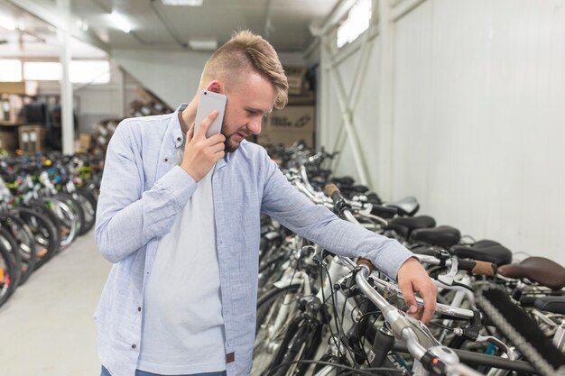 Man looking at bicycle while talking on cellphone in shop