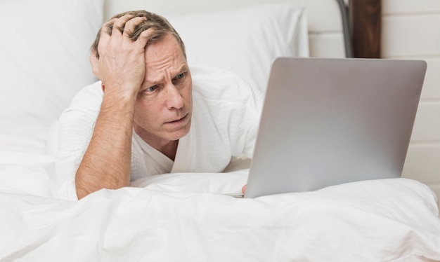 Мужчина ищет обеспокоен на своем ноутбуке в постели