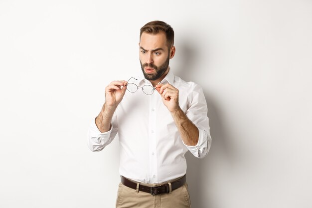 Man looking confused at his glasses, standing in office clothing