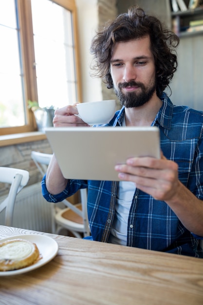 コーヒーカップを持ちながら男は、デジタルタブレットを見て