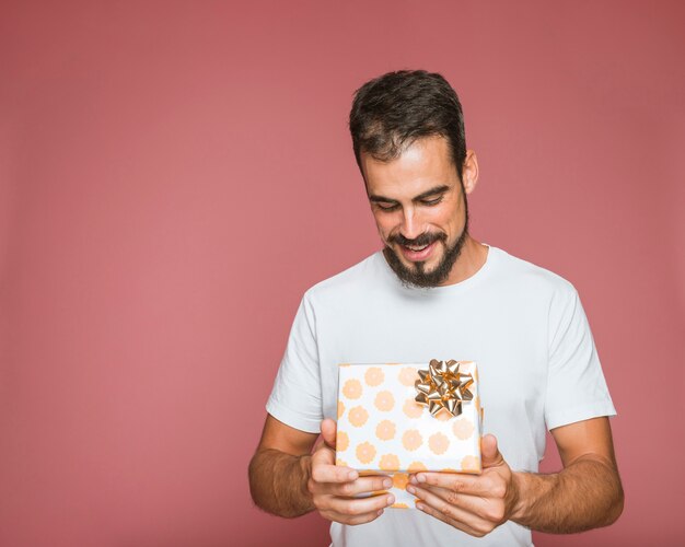 Man looking at floral gift box with golden bow against colored background