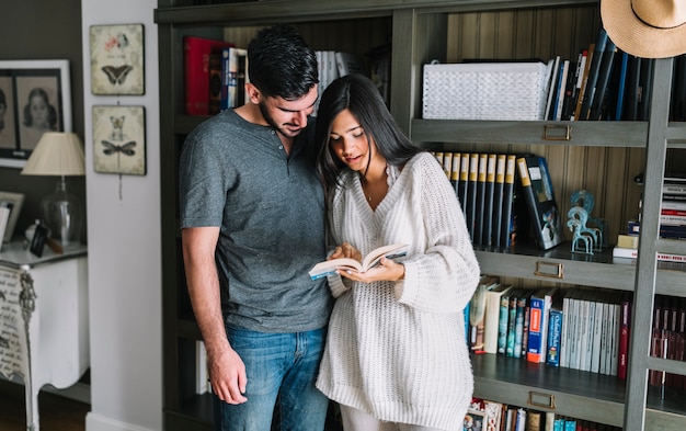 Man looking at girlfriend reading book standing in front of bookshelf