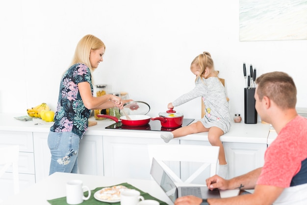 Человек, глядя на свою жену и дочь, работающих на кухне