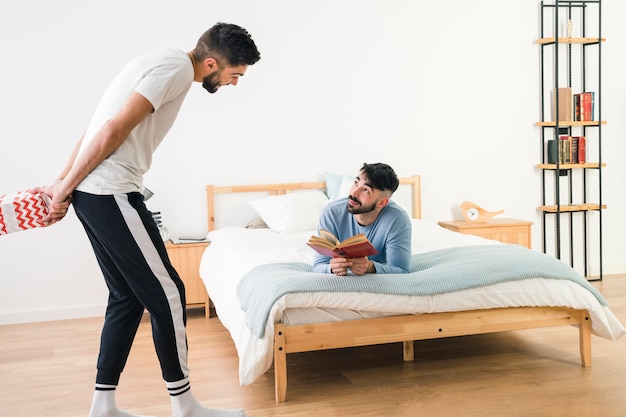 Man looking at his boyfriend standing and holding gift box behind his back