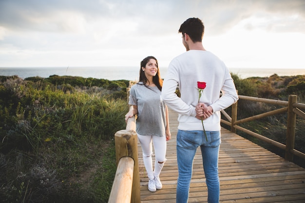 Man looking at his girlfriend while hiding a rose on his back