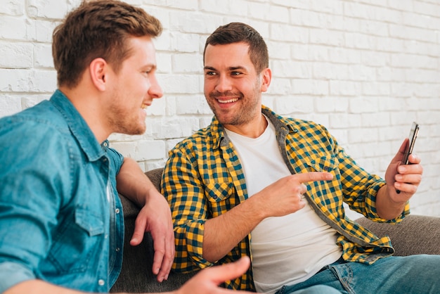 Man looking at his smiling friend pointing his finger on mobile phone