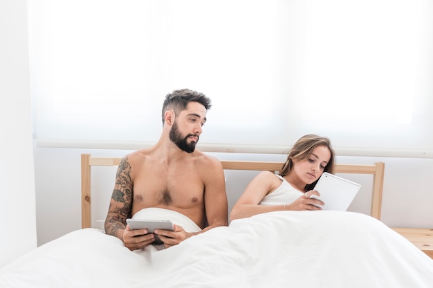 Free photo man looking at his wife using digital tablet on bed