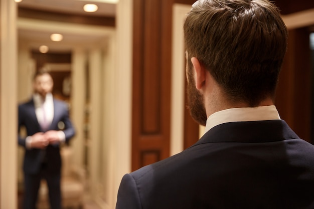 Free photo man looking in mirror wearing suit