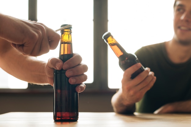 A man looking at a person opening brown beer bottle in restaurant