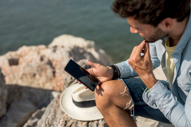 Foto gratuita uomo che guarda su smartphone in riva al mare