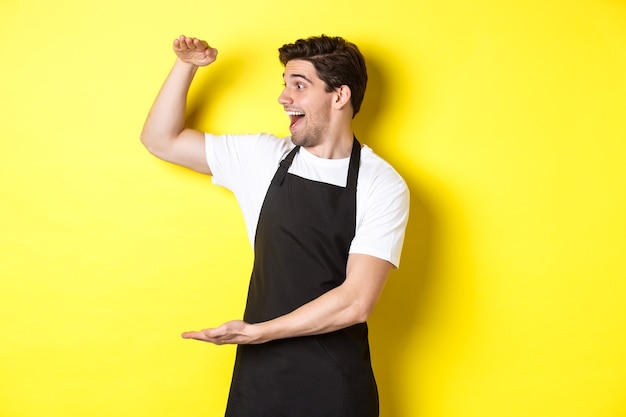 Man looking surprised at something large standing in black apron against yellow background