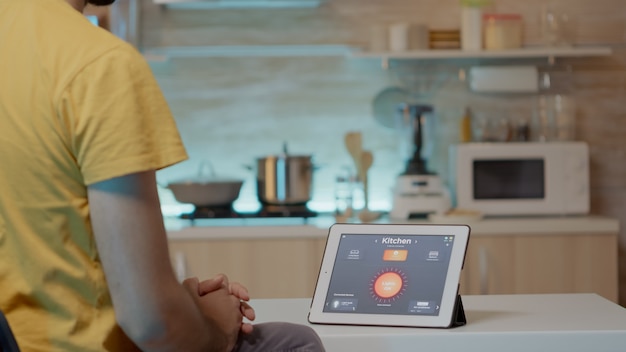 높은 조명으로 조명을 제어하는 식탁에 지능형 소프트웨어가 설치된 태블릿을 보고 있는 남자