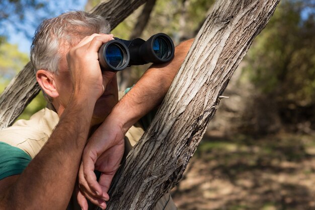 Man looking through binocular by tree