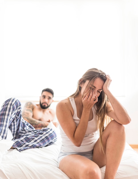 Man looking at upset woman sitting on bed