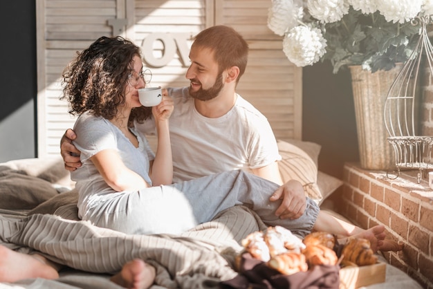 Man looking at woman sitting on man's lap drinking coffee at morning