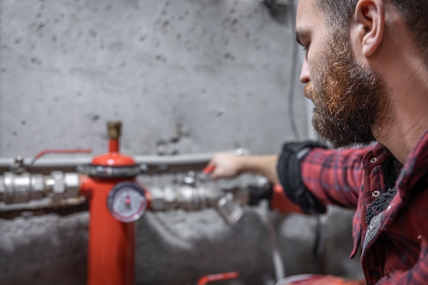 The man looks at the faucet, pipes, valve, pressure meter.