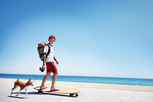 Man looks like a santa ride longboard on the beach with his dog