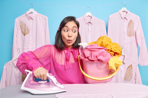 man looks at pile of laundry in bucket going to do ironing busy with domestic chores wears pink blouse poses on blue 