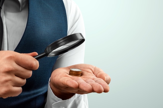 Premium Photo | A man looks through a magnifying glass at a stack of coins  in his palm. small salary, bankruptcy.