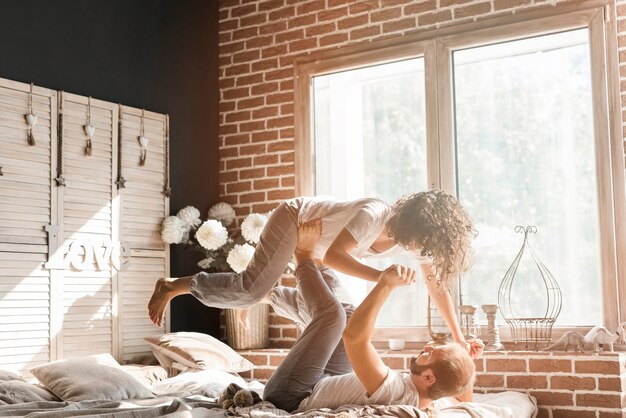 Man lying on bed carrying her wife on his feet near the window