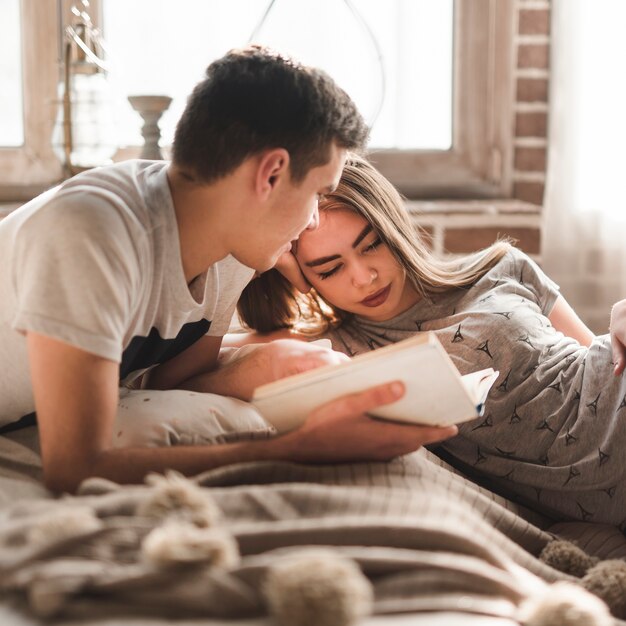 Man lying on bed looking at woman holding book in hand at home