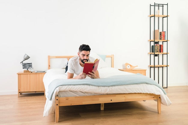 Man lying on bed reading the book in the bedroom