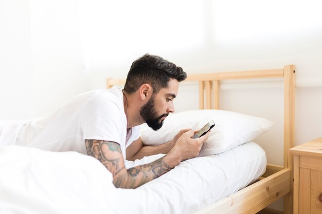 携帯電話を使ってベッドに横たわっている男