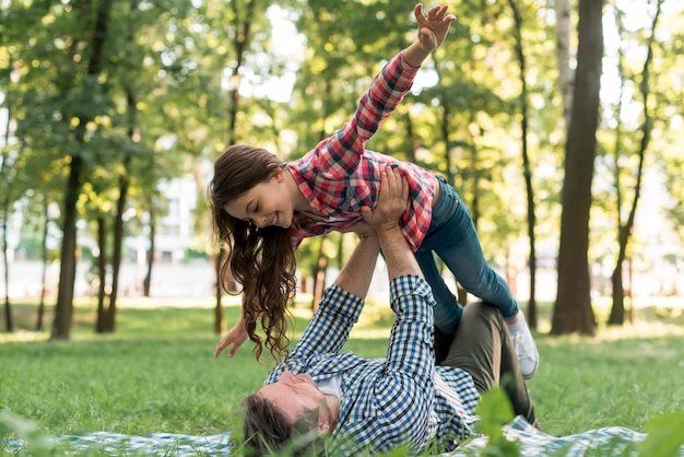 Man lying on blanket carrying his daughter in garden