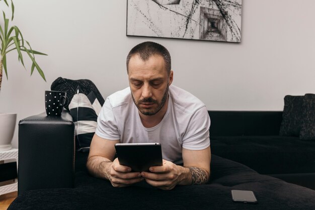 Man lying on couch and using tablet