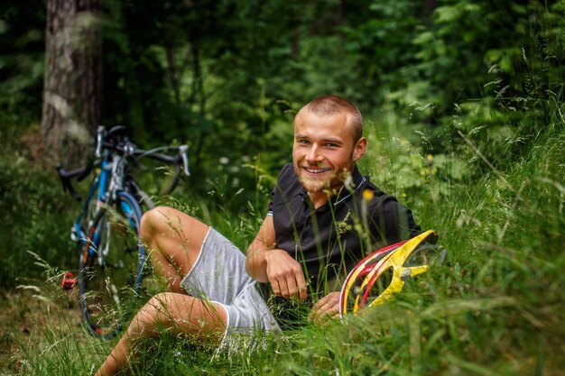 森の草の上に横たわっている男。背景に2台の自転車。
