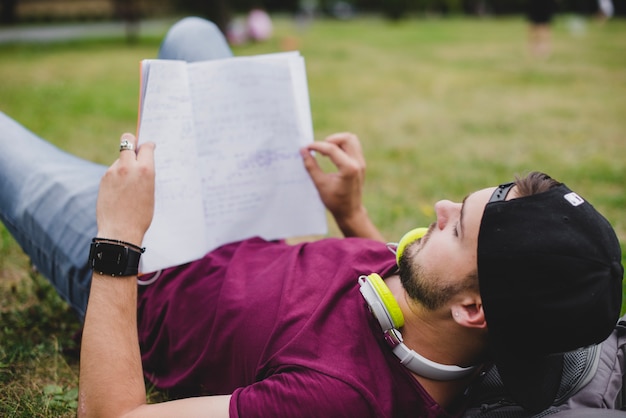 Free photo man lying on grass reading notebook