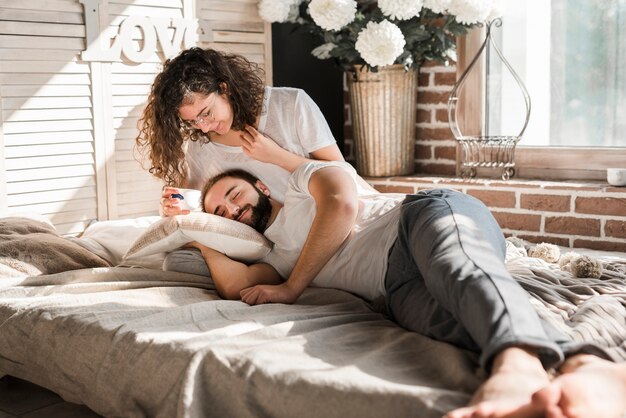自宅のベッドで一杯のコーヒーを保持している女性の膝の上に横たわる男
