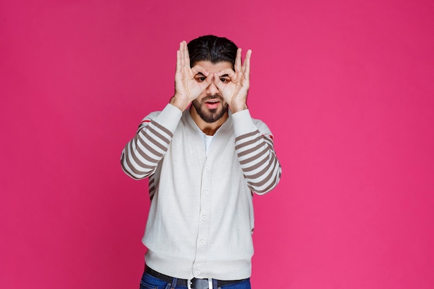 Uomo che fa la faccia e gli occhi del gufo con le dita.