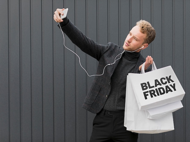 Free photo man making a selfie while holding black friday shopping bags