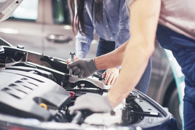 A man mechanic and woman customer look at the car hood and discuss repairs