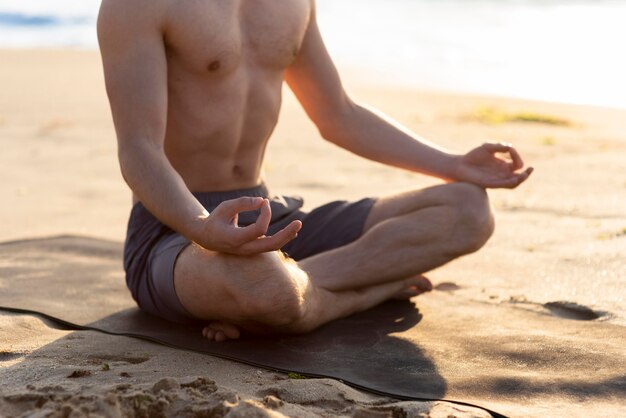 Man meditating shirtless on the beach