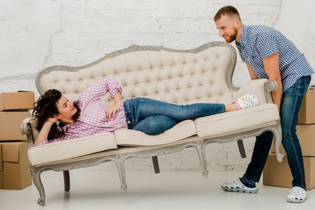 Free photo man moving sofa with lying woman