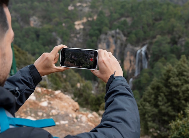 Человек на природе фотографирует с помощью мобильного телефона