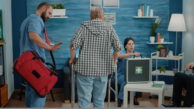 Man nurse supporting senior woman using walk frame at nursing home facility. Medical assistant helping disabled patient walk for recovery. Old person getting help with transportation