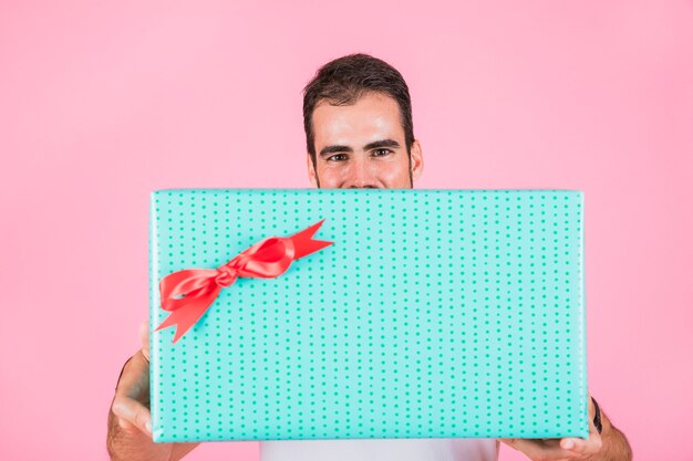 Человек, предлагающий прямоугольную подарочную коробку, стоящую на розовом фоне