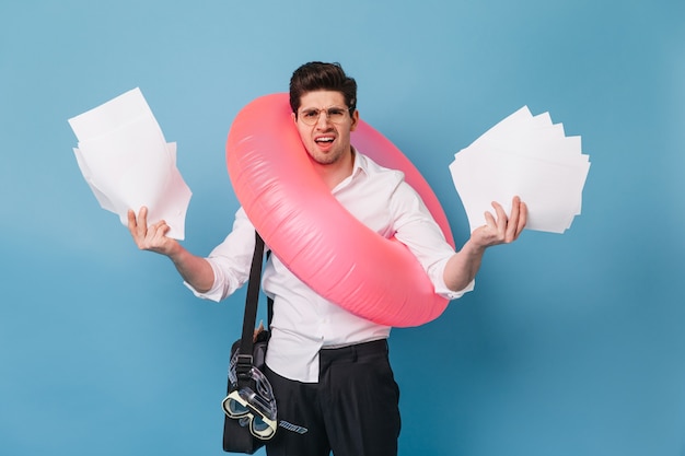 Free photo man in office clothes throws out his work papers, going on vacation with inflatable circle.