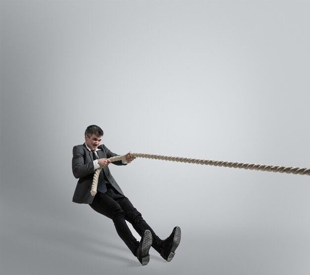 Man in office clothes training with ropes on grey background.