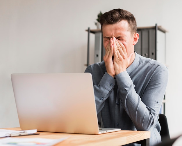 Man in office during pandemic holding his nose