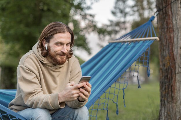 Бесплатное фото Человек в гамаке, слушая музыку в наушниках с смартфона