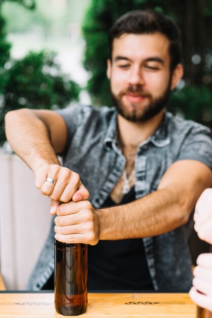 テーブルにアルコールのボトルを開いている男