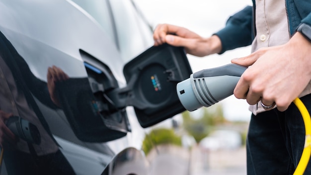 Man opening cars charge socket and holding charger at charge station