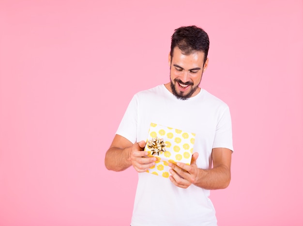 Man opening yellow polka dot gift box in hand over pink background