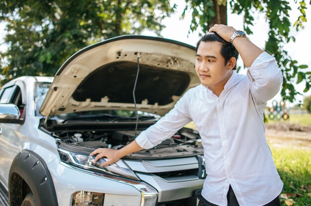 A man opens the hood of a car to repair the car due to a breakdown.